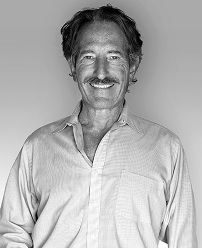 A black and white portrait of a smiling man with a mustache and dark, wavy hair, wearing a light collared shirt.